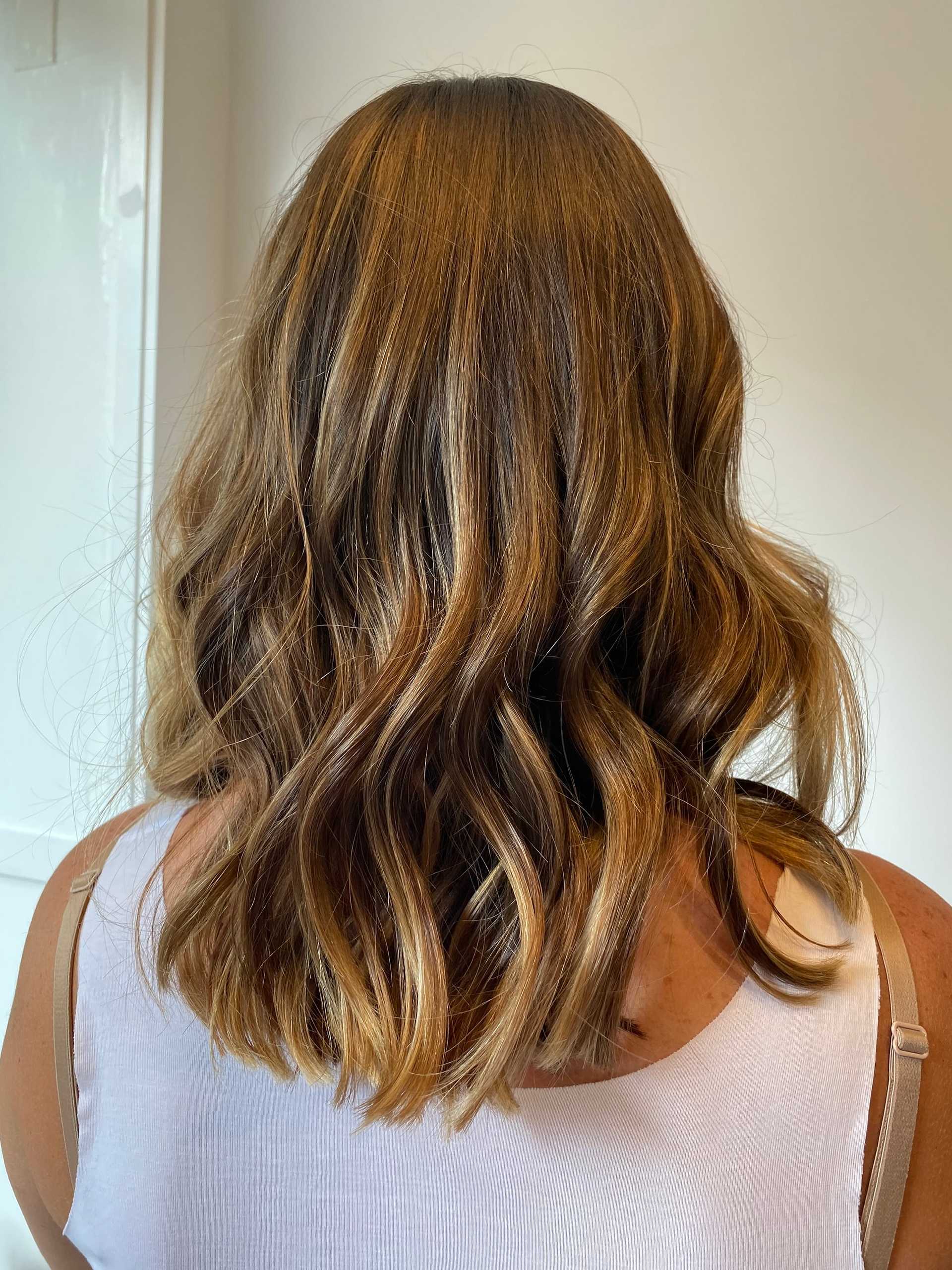 Wavy, shoulder-length hair with light brown and blonde highlights, worn by a person facing away.