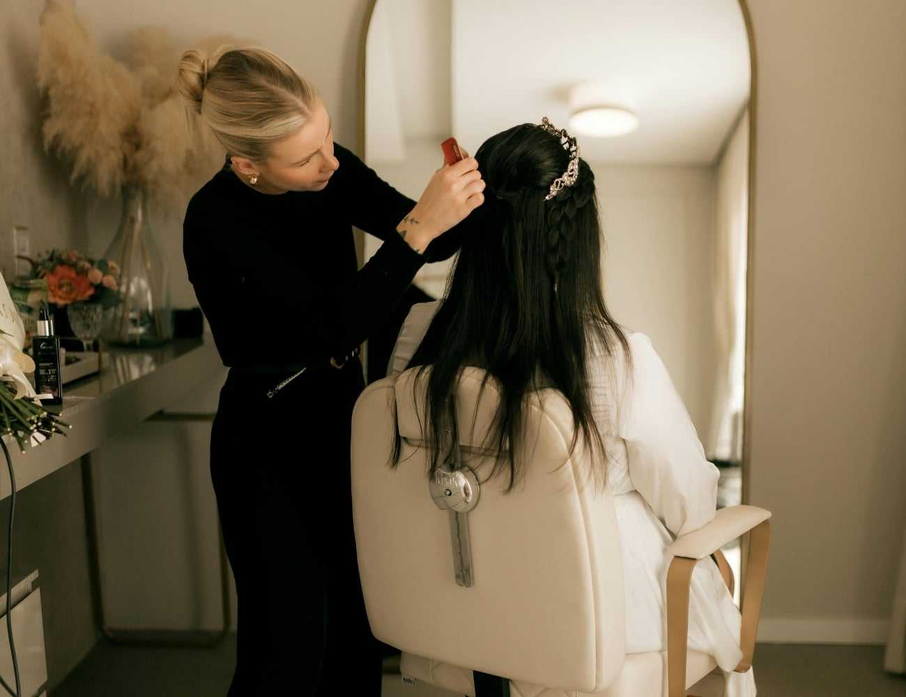 Hair stylist working on a woman's bridal hairstyle in a salon chair.