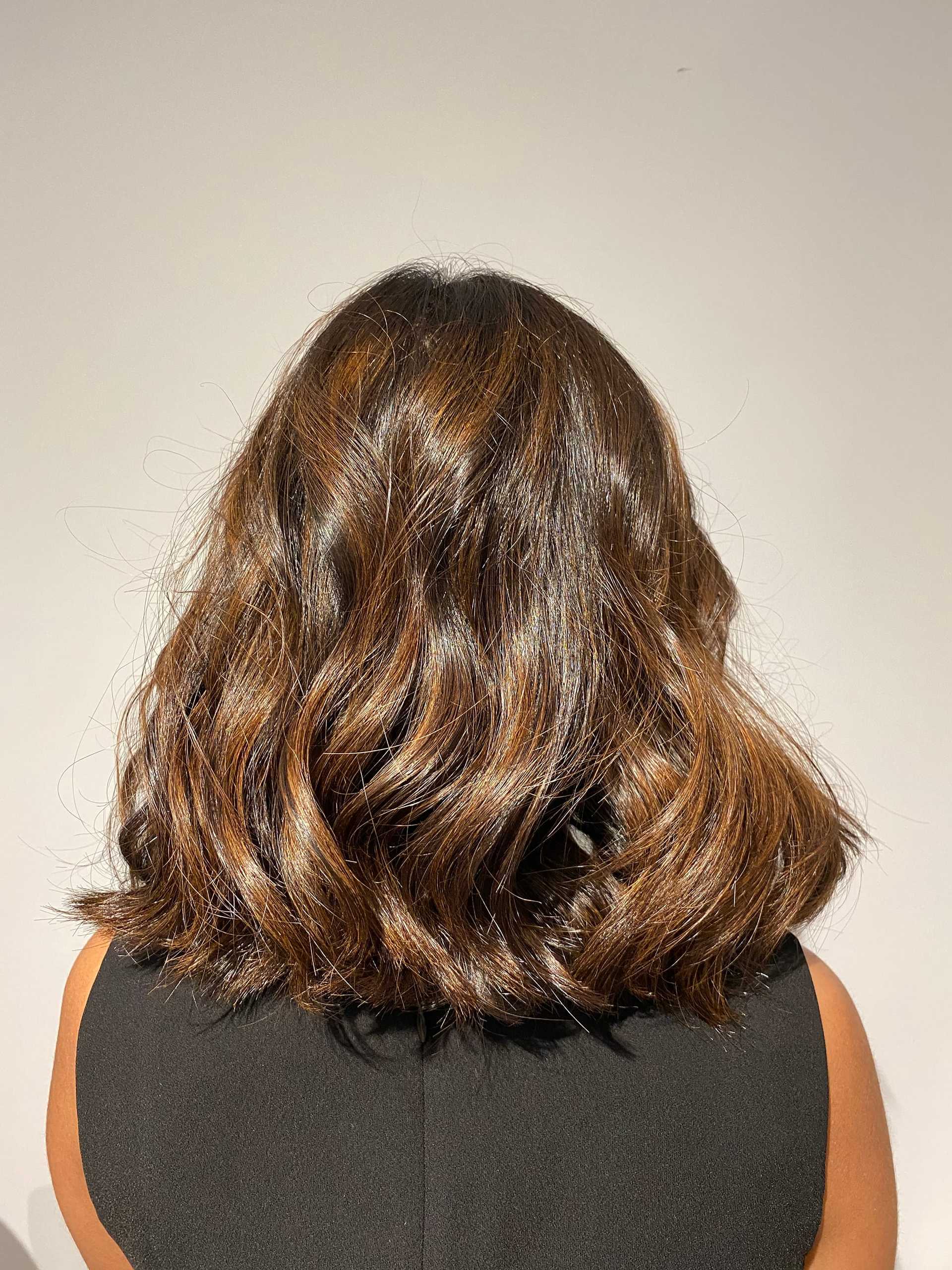 Woman with shoulder-length brown hair, seen from the back, wearing a black sleeveless top.