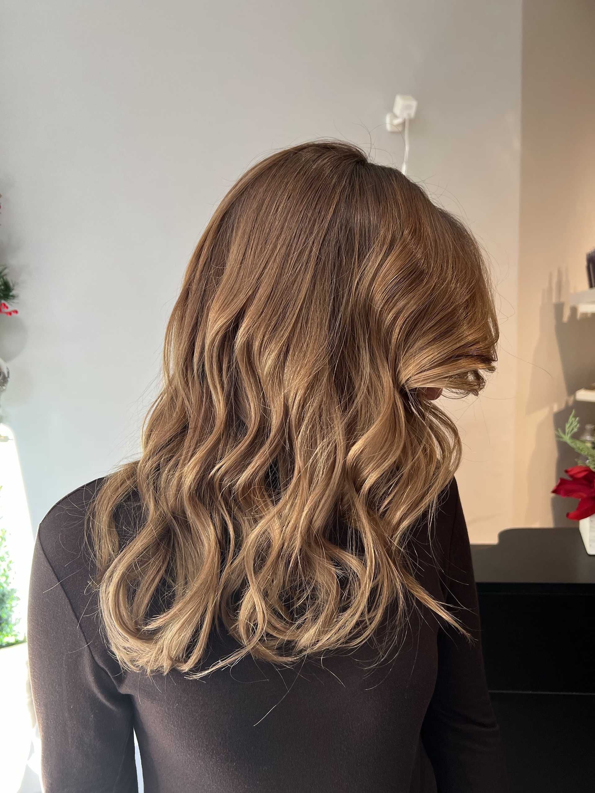 Woman with wavy, caramel-colored hair in a salon setting.