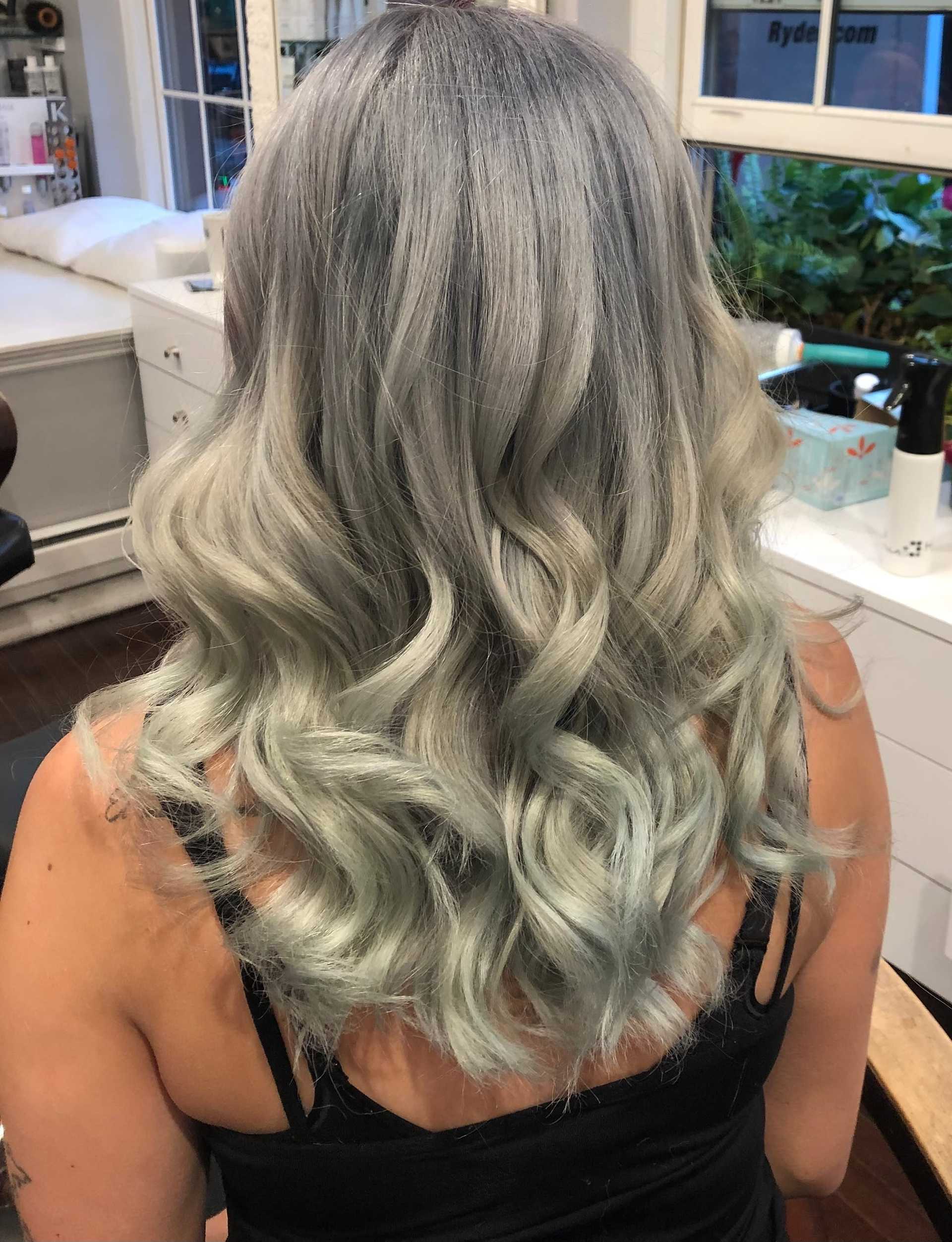 Wavy silver-blue hair on a person in a salon setting with styling products around.